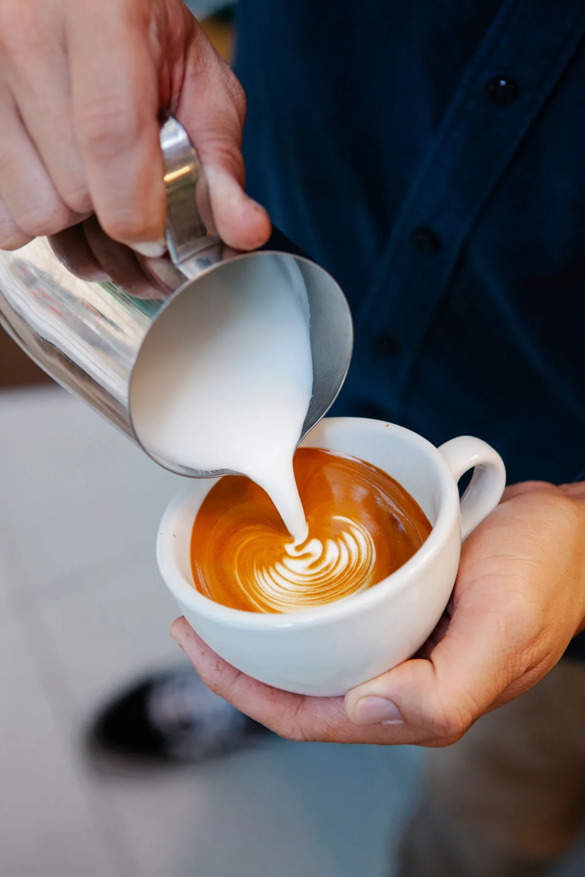 A barista pouring milk from a metal pitcher into coffee