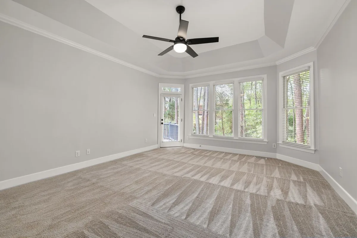 A bright carpeted room with large windows and a ceiling fan