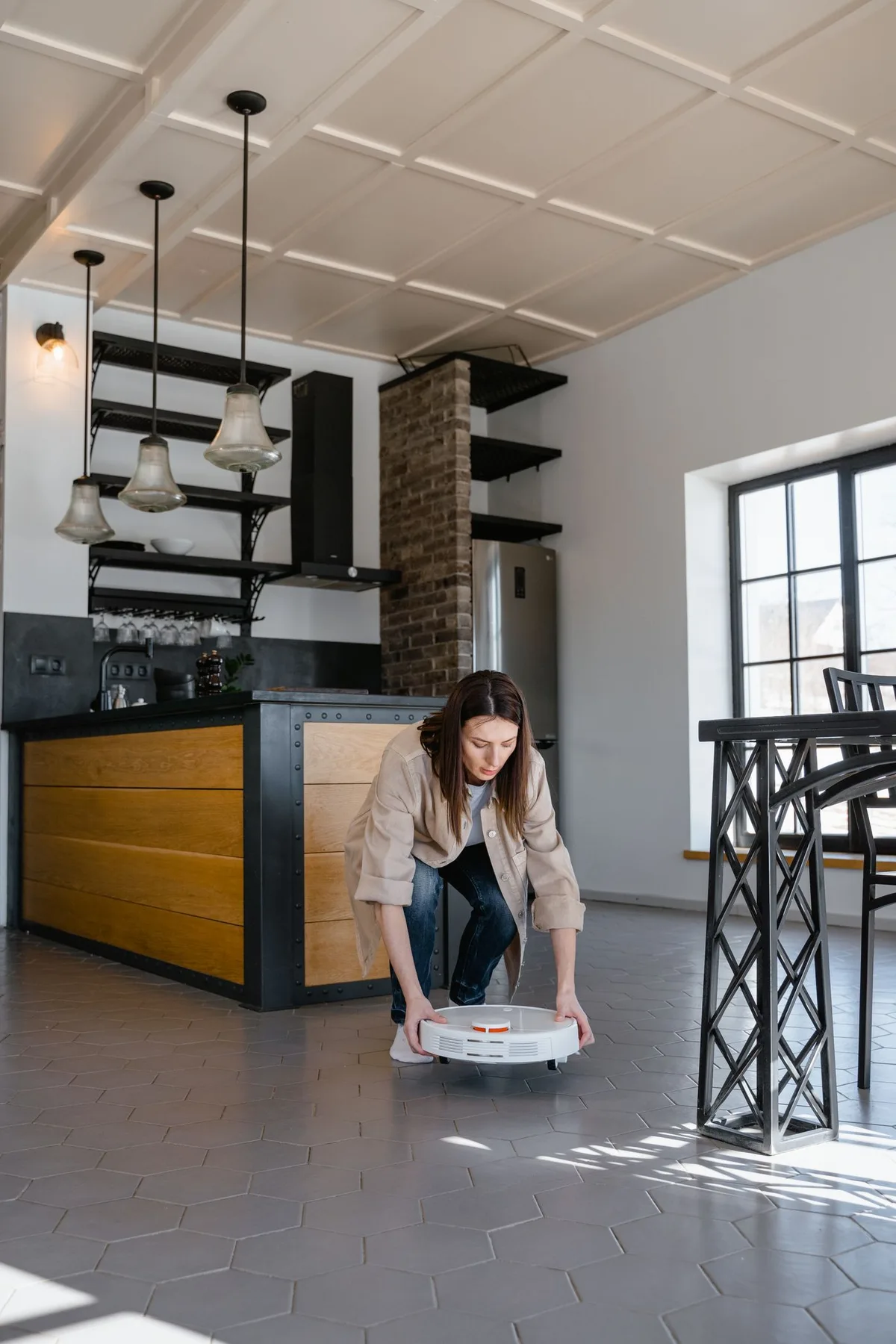 A woman placing a robot vacuum on the floor in a kitchen