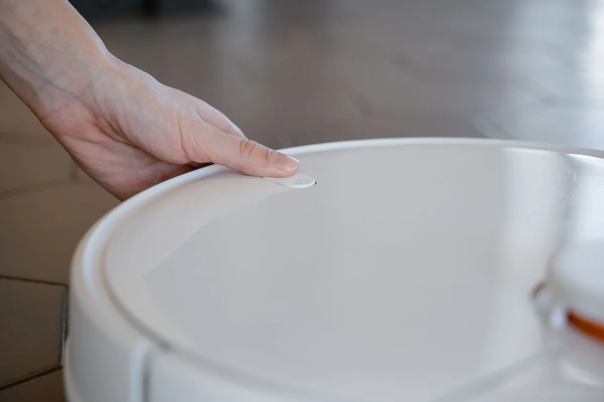 A hand operating the controls of a white robot vacuum