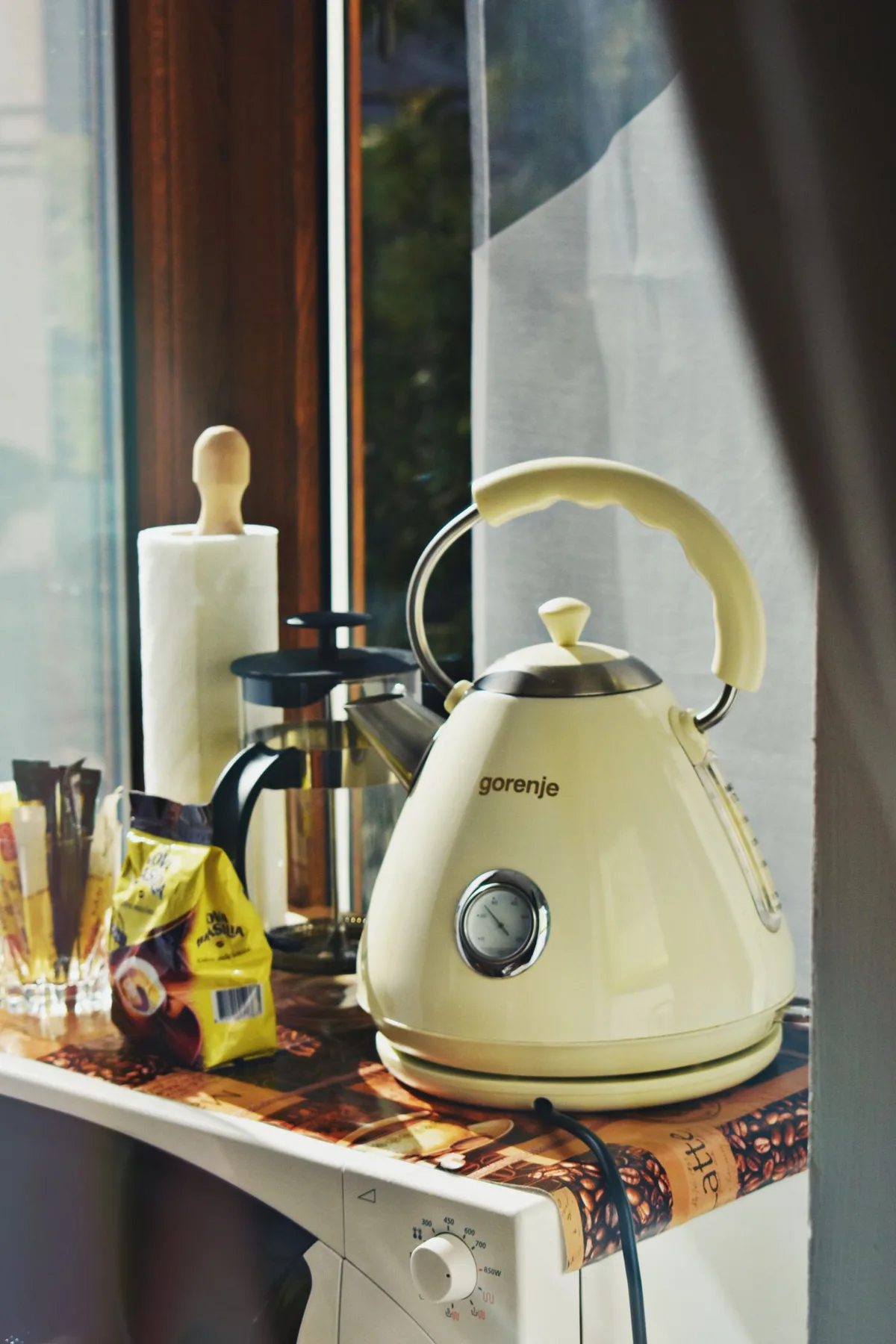 A white electric kettle beside coffee accessories on a counter
