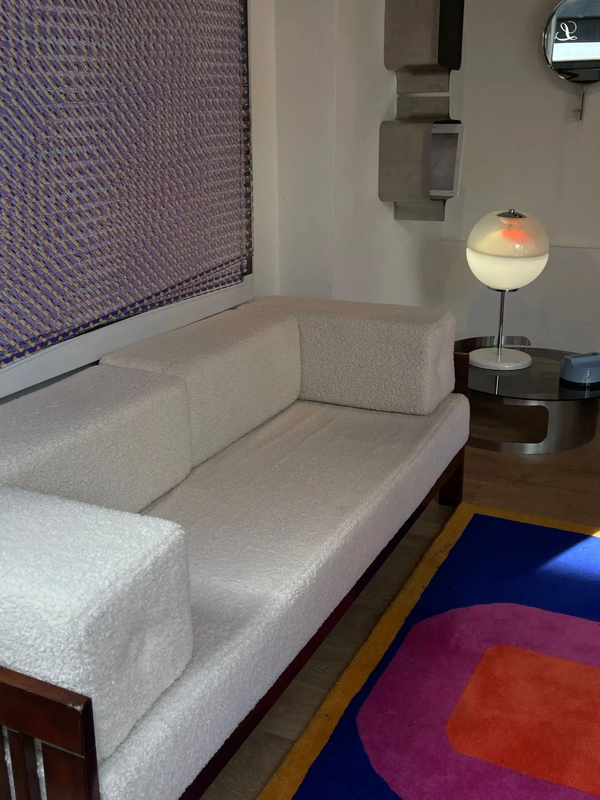 A cream sofa beside a colorful geometric rug and a round table lamp